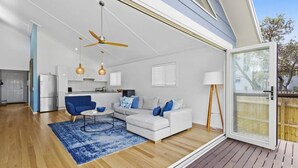 A modern living room with a white sofa, blue armchair, and a dining area with a kitchen in the background.