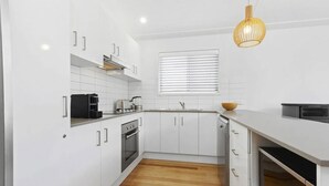 A modern kitchen with white cabinetry, a built-in oven, a coffee machine, and a wooden bowl on the counter.