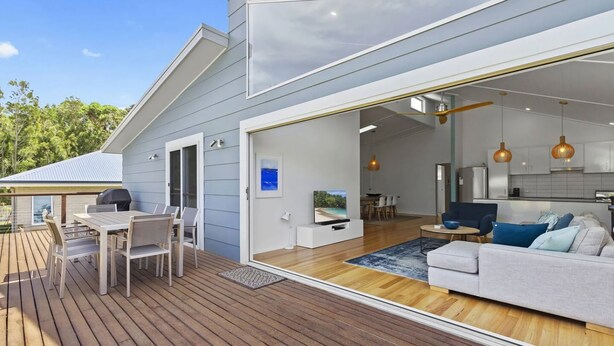 A modern house with a deck, a dining area, a living room with a sofa, and a kitchen.