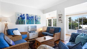 Un salon moderne avec des meubles en osier, un téléviseur et des œuvres d’art accrochées aux murs.