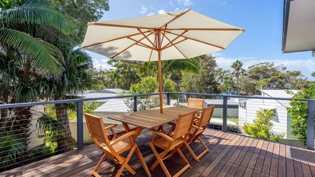 Une terrasse en bois avec une table et des chaises, un parasol et une vue sur des maisons et des arbres.