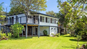 Une maison à deux étages dotée d’un balcon, entourée d’une pelouse bien entretenue et de divers arbres.