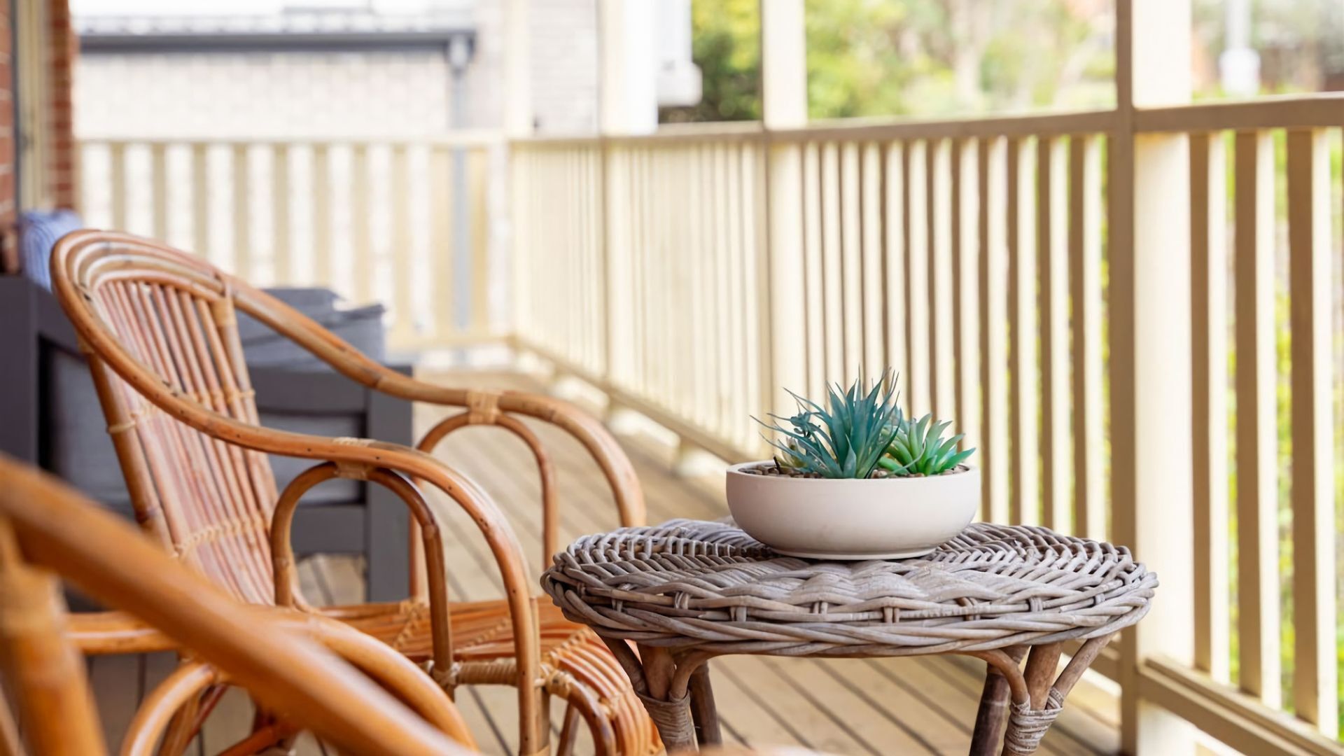 A wicker chair and a small table with a potted plant on a wooden deck.