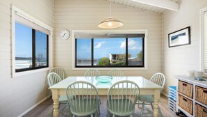 Un coin repas avec une table et des chaises, une horloge au mur et une vue sur l’océan grâce à de grandes fenêtres.