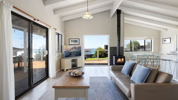 Un salon spacieux avec un grand canapé, une table basse en bois et un téléviseur. On y trouve également une cheminée et un balcon avec vue sur la mer.