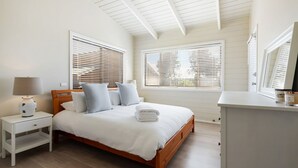 Une chambre à coucher avec un lit en bois, du linge de lit blanc et deux tables de chevet avec des lampes.
