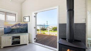 Une pièce avec un téléviseur posé sur un meuble, une cheminée et une porte donnant sur un balcon avec vue sur l’océan.