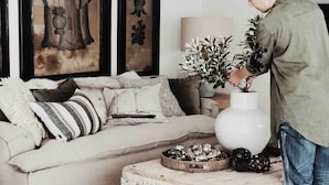 Un salon comprenant un canapé, des coussins, un grand vase blanc et une petite table ornée d’objets décoratifs.
