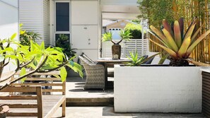 A patio area with a wooden bench, a wicker chair, and a concrete planter with a large plant. - The Tasman Secret, moments to Manyana Beach (Manyana)