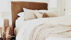 A neatly made bed with a brown headboard, white bedding, and a small wooden side table with a candle. - The Tasman Secret, moments to Manyana Beach (Manyana)
