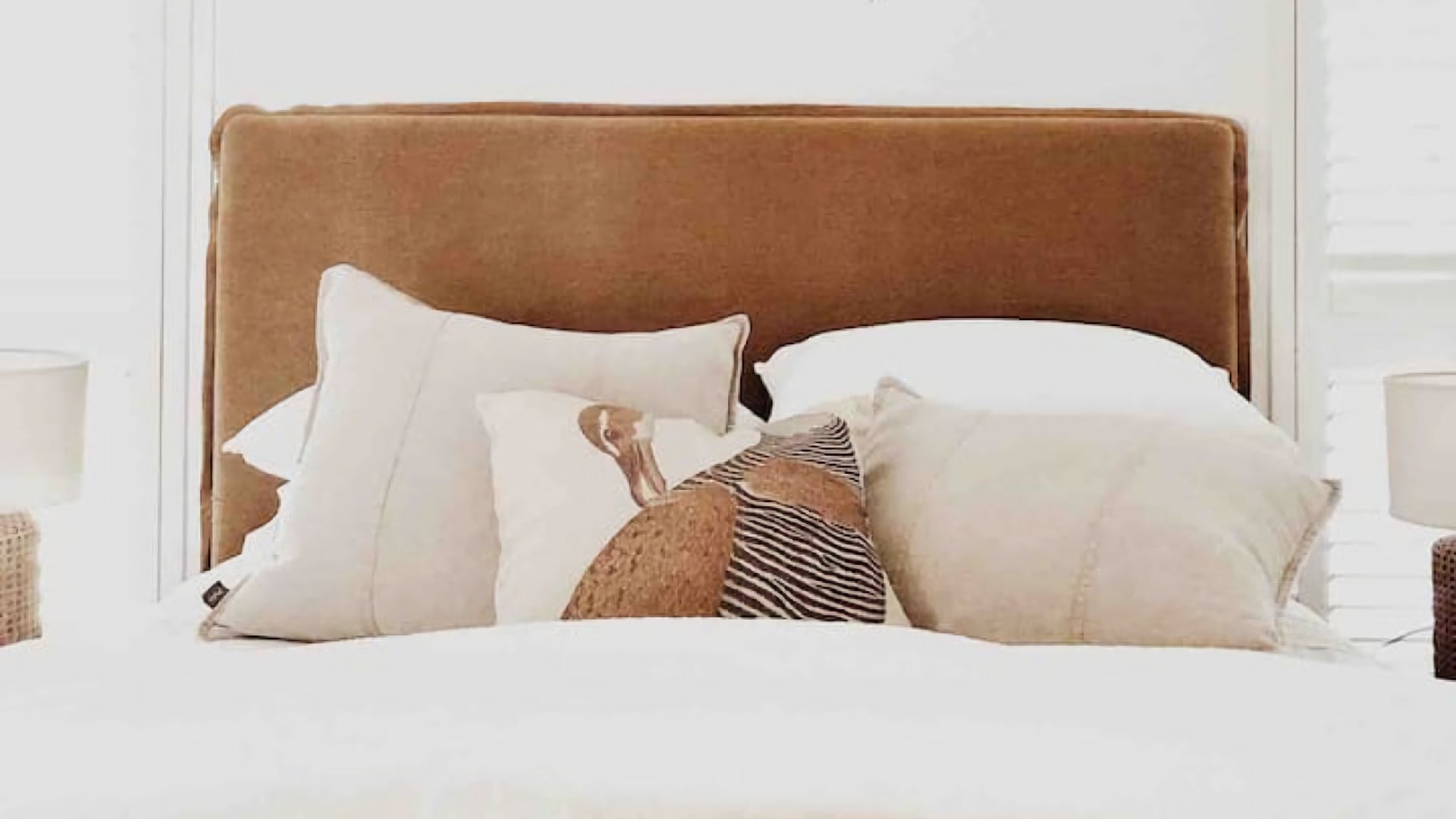 A bed with a brown headboard, white bedding, and multiple pillows including a zebra-patterned one.