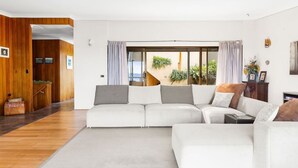 A modern living room with a sectional sofa, a wooden floor, and a view of a staircase and greenery outside.