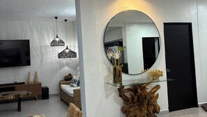 Un salon moderne avec un téléviseur à écran plat, des meubles en bois, une table basse en verre et un miroir rond accroché au mur.