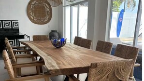 Un coin repas avec une table en bois et des chaises en osier, un bol décoratif et une grande fenêtre donnant sur l’extérieur.
