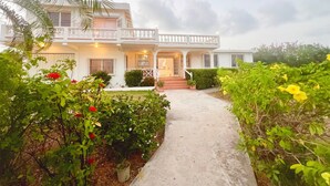 A two-story house with a balcony, a front porch, and a pathway leading to the entrance. - Bow Green Villa in Redezvous Bay Steps From Rendezvous Beach (West End)