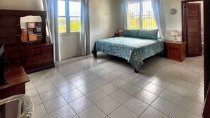 A bedroom with a bed, a dresser, a chair, and a ceiling fan. - Bow Green Villa in Redezvous Bay Steps From Rendezvous Beach (West End)