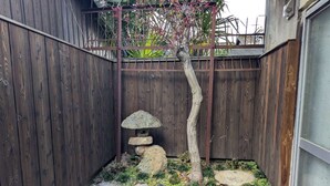 Ein kleiner Gartenbereich mit Holzpforte, Stein Laterne und Baum mit rosa Blüten.