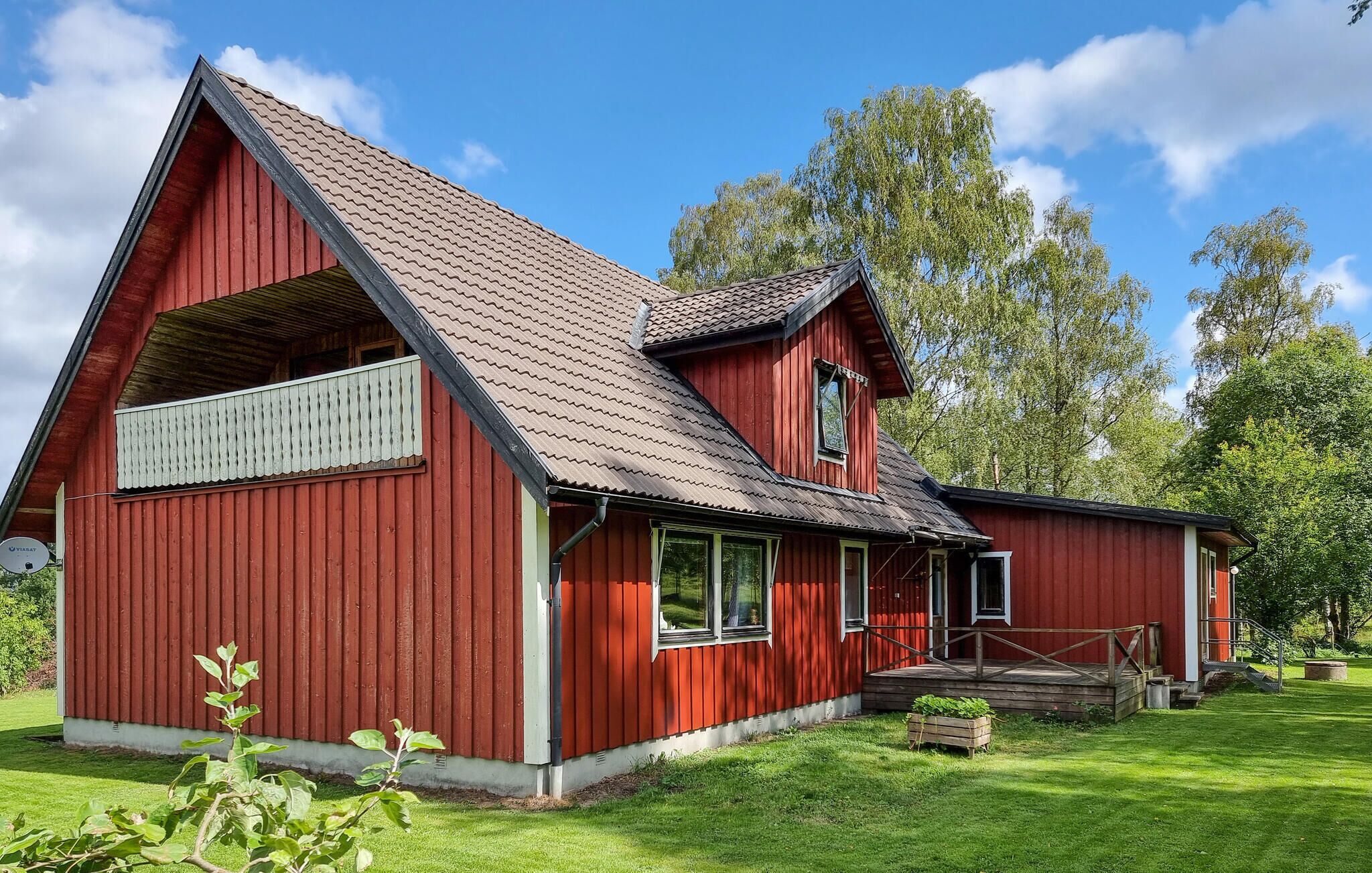 Ein rotes Holzhaus mit geneigtem Dach, einem großen Fenster und einer Veranda.