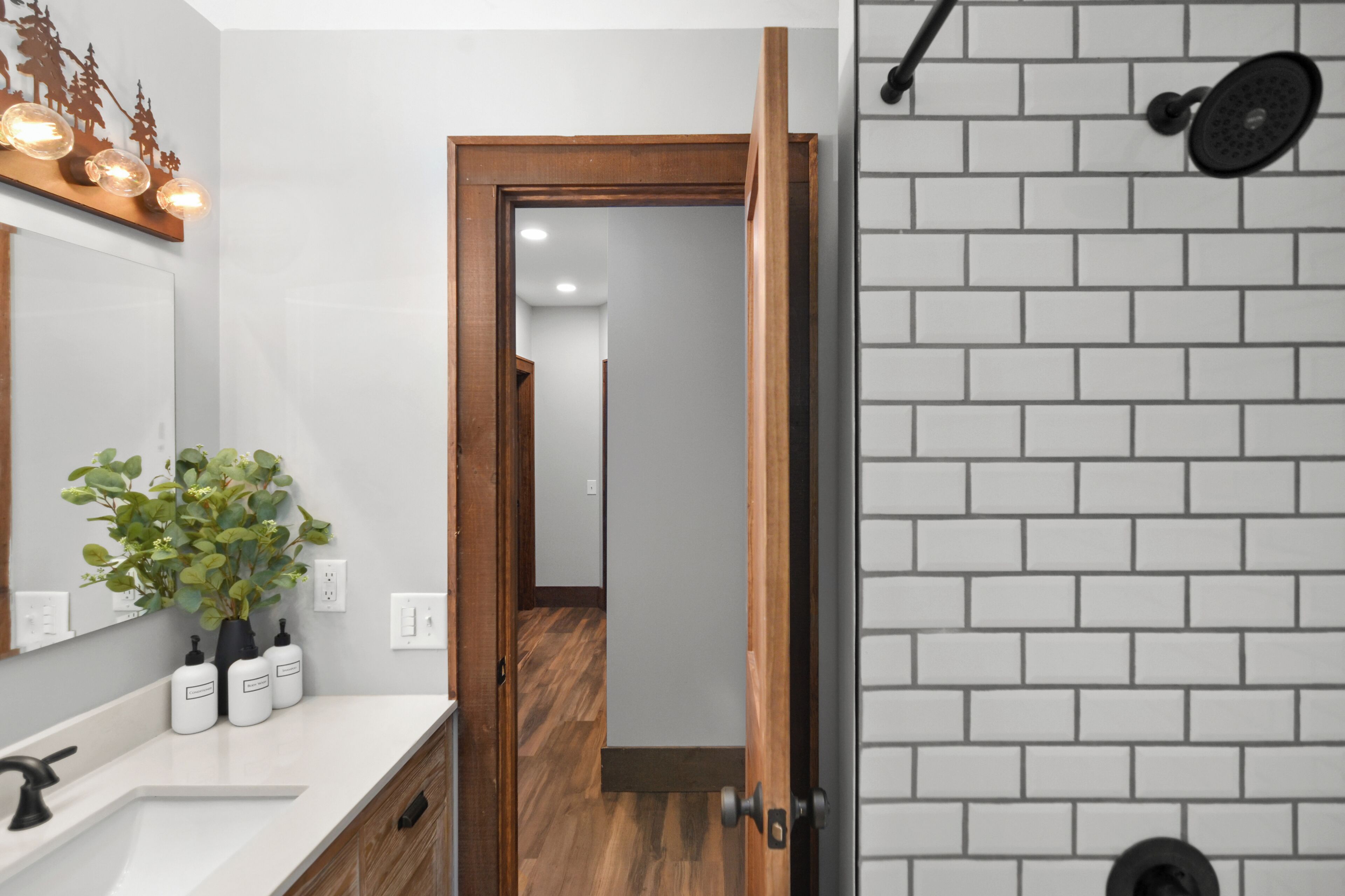 A bathroom with a white sink, wooden door, and a shower area with a white tiled wall.
