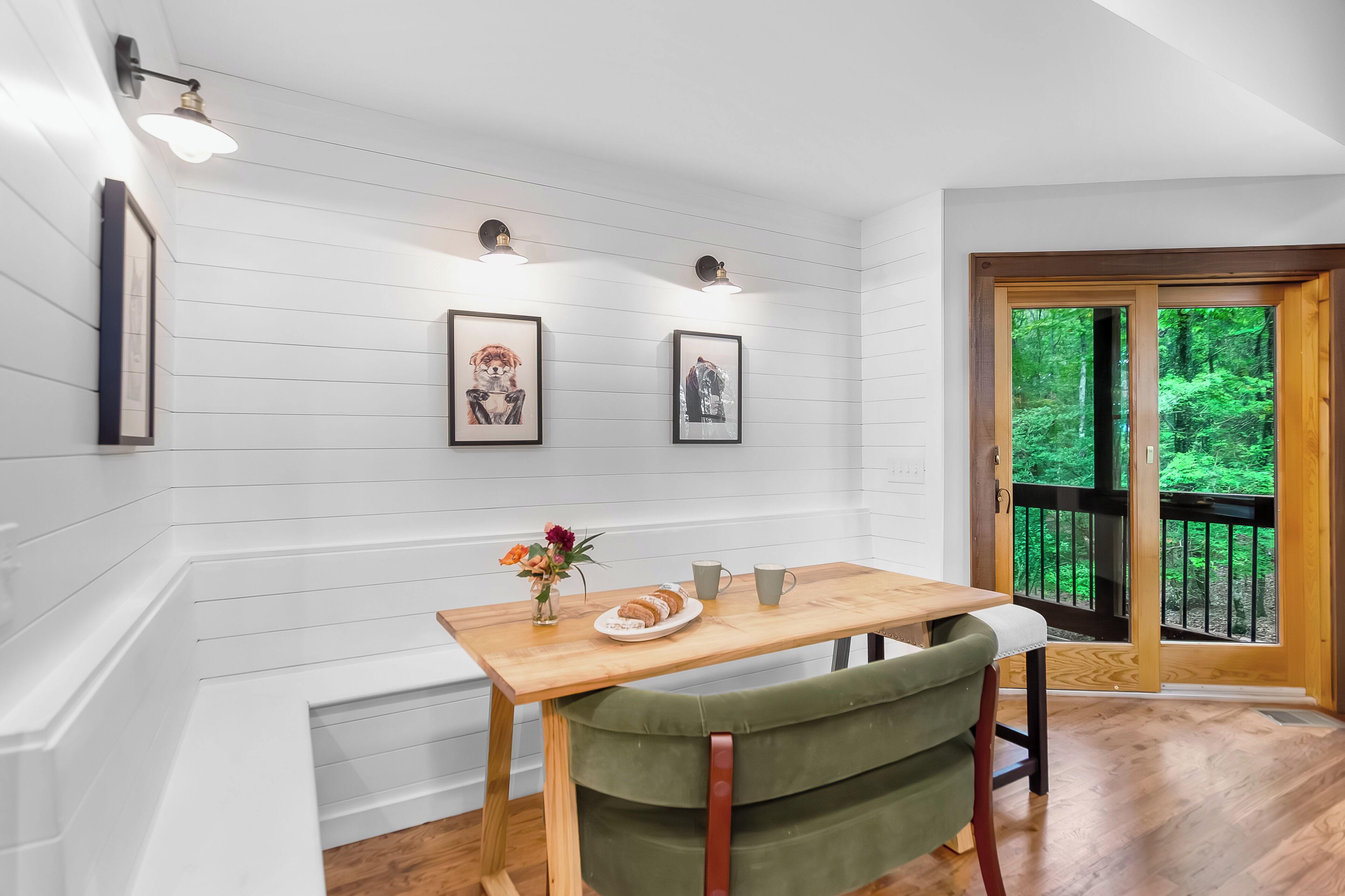 A dining area with a wooden table, a green upholstered chair, and framed pictures on the wall.