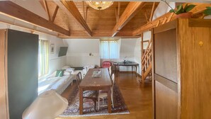 Una habitación espaciosa con techo de madera, una mesa de comedor con sillas, un sofá y un televisor colgado en la pared.
