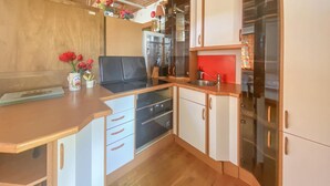 Una cocina compacta con armarios blancos, estufa negra y salpicadero rojo.