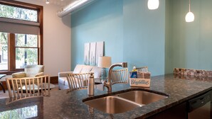 A kitchen with a granite countertop, stainless steel sink, and a dishwasher. There is a window with a view of trees, a chair, and a couch in the background. - Downtown Holland Loft  The "Erie"| 1BR, Walking Distance to Breweries & Dining (Holland)