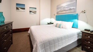 A hotel room with a large bed, a dresser, a nightstand, and a painting on the wall. - Downtown Holland Loft  The "Erie"| 1BR, Walking Distance to Breweries & Dining (Holland)
