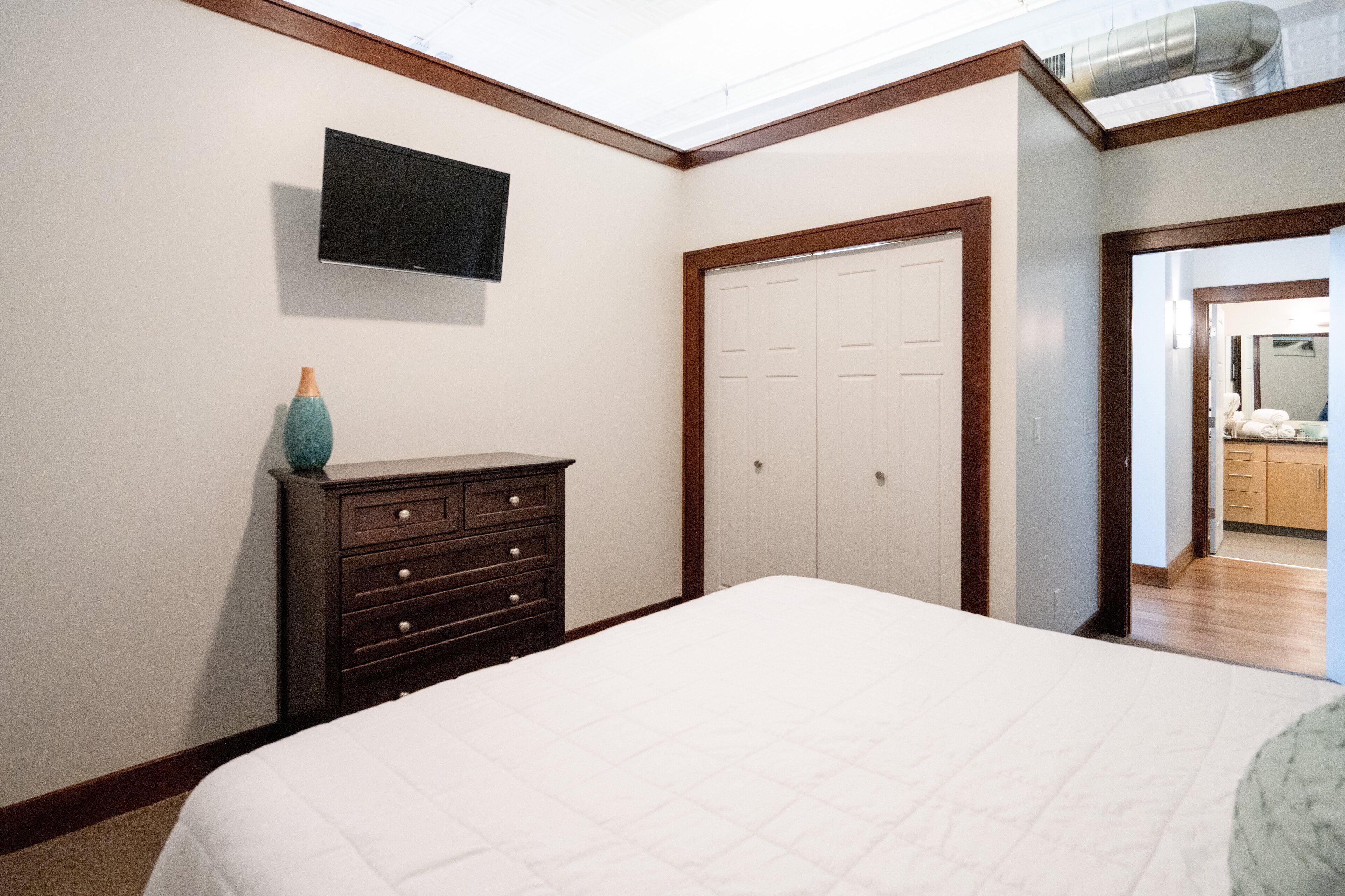 Ein Schlafzimmer mit einem Bett, einem Schminktisch, einem an der Wand befestigten Fernseher und einem Kleiderschrank.