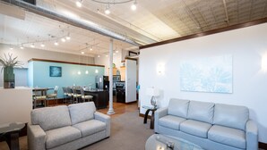 A modern living room with two grey sofas, a glass coffee table, and a dining area with chairs and a table.