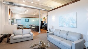 A spacious living room with two grey sofas, a glass coffee table, and a dining area in the background.