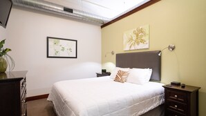A neatly arranged bedroom with a bed, bedside tables, a lamp, and artwork on the walls.