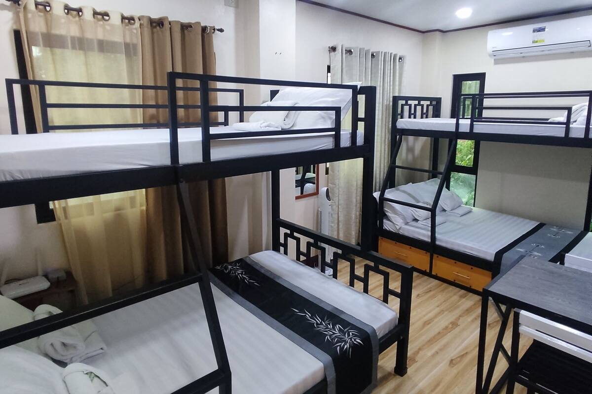 A dormitory room with bunk beds, a desk, and an air conditioning unit.