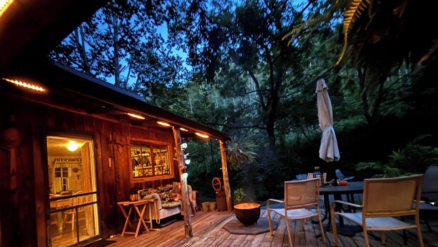 A wooden deck with outdoor furniture, a bar area, and a view of the surrounding forest. - Authentic Appalachian 200yr old Riverfront Farmhouse Cabin in Pittman Center.  (Sevierville)