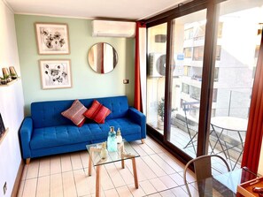 A living room with a blue sofa, a glass coffee table, a round mirror, and a view of the outside. - Comfortable, equipped stay in a prime area (Las Condes)