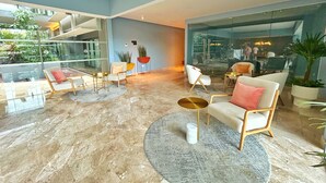 A modern lobby with a marble floor, seating area with sofas and chairs, potted plants, and a glass wall offering a view of the outside. - SINGULAR DREAM (Playa del Carmen)