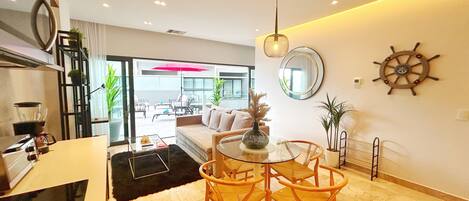 A modern living room with a round glass table, wooden chairs, a sofa, and a coffee machine.