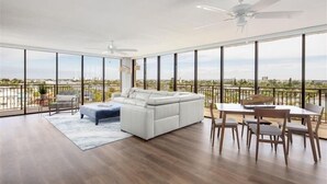 A spacious living room with a white sofa, a dining table with chairs, and a balcony with a view of the city.