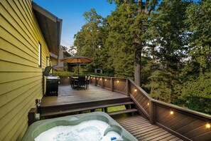 Una terraza de madera con un jacuzzi, mobiliario exterior e iluminación con luces colgantes.