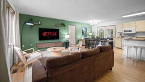 A modern living room with a large flat-screen TV, a sofa, a dining area, and a kitchen with a microwave.