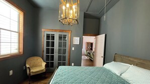 A bedroom with a bed, a chair, a wardrobe, and a chandelier.