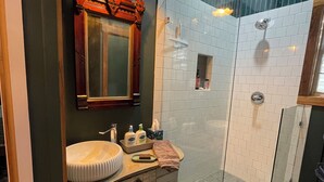 A bathroom with a wooden vanity, a large mirror, a glass-enclosed shower, and a patterned floor.