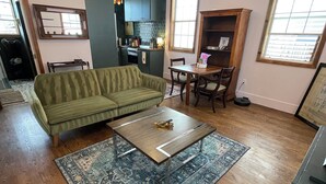 A living room with a green sofa, a coffee table, a rug, and a dining area with chairs and a table.
