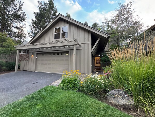 A single-story house with a garage, surrounded by a well-maintained garden with various plants and flowers. - Family Friendly Fremont Crossing Home, 3 Kings, Bunk Room, Hot Tub, SHARC Passes (Sunriver)