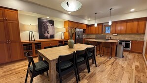 A modern kitchen with wooden cabinets, a central island with chairs, a refrigerator, and a microwave. - Family Friendly Fremont Crossing Home, 3 Kings, Bunk Room, Hot Tub, SHARC Passes (Sunriver)