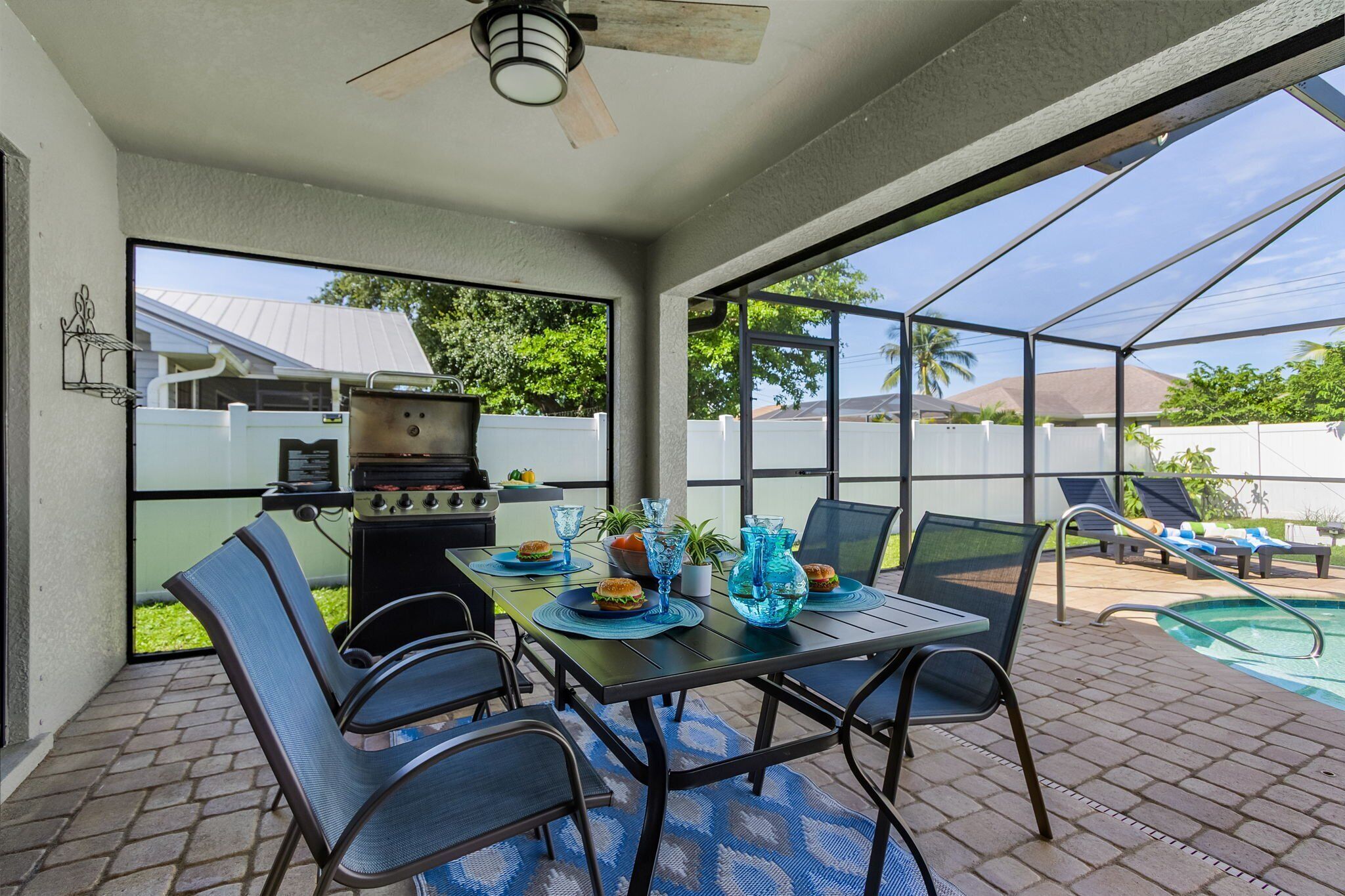 An outdoor patio with a table set for dining, a grill, and a pool area.