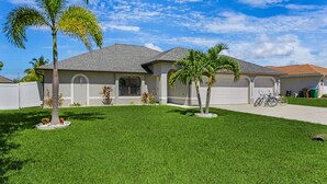 A residential house with a well-maintained lawn, two palm trees, and a garage. - Sun, Fun & Relaxation Await with Heated Pool, Lanai & Spacious Comfort – K La Vie - Roelens (Cape Coral)