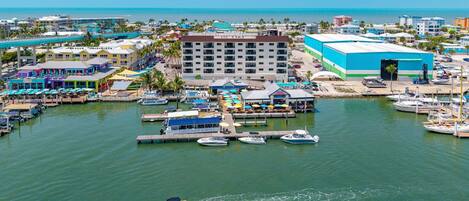 A marina with boats docked, a large building with a blue facade, and a waterfront restaurant area.