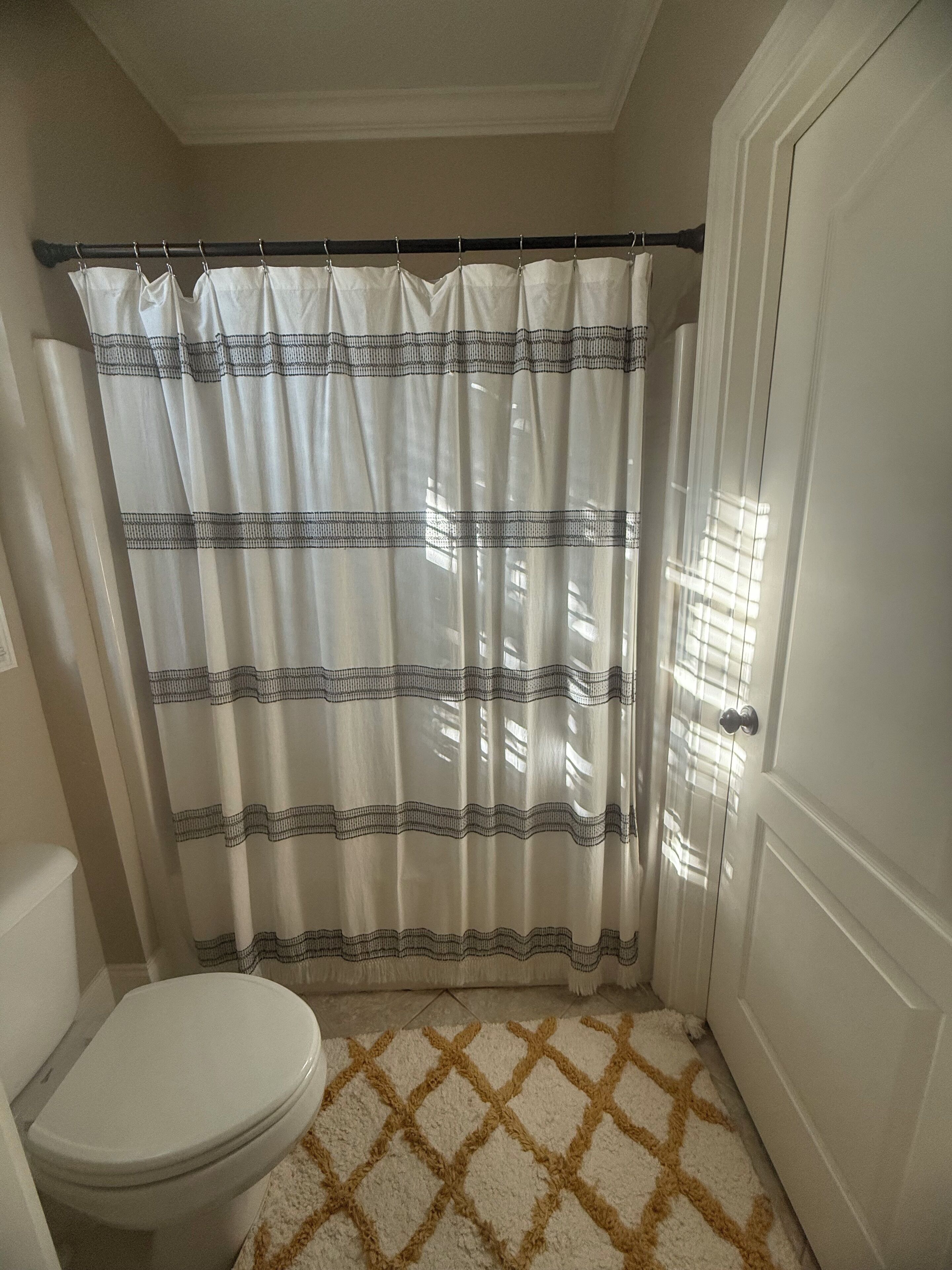 A bathroom with a toilet, a shower curtain, and a patterned rug.