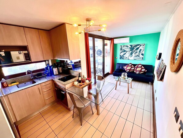 A compact kitchen with a dining area, a sofa, and a large window. - Las Condes Apt | Prime Location + Fully Equipped (Las Condes)